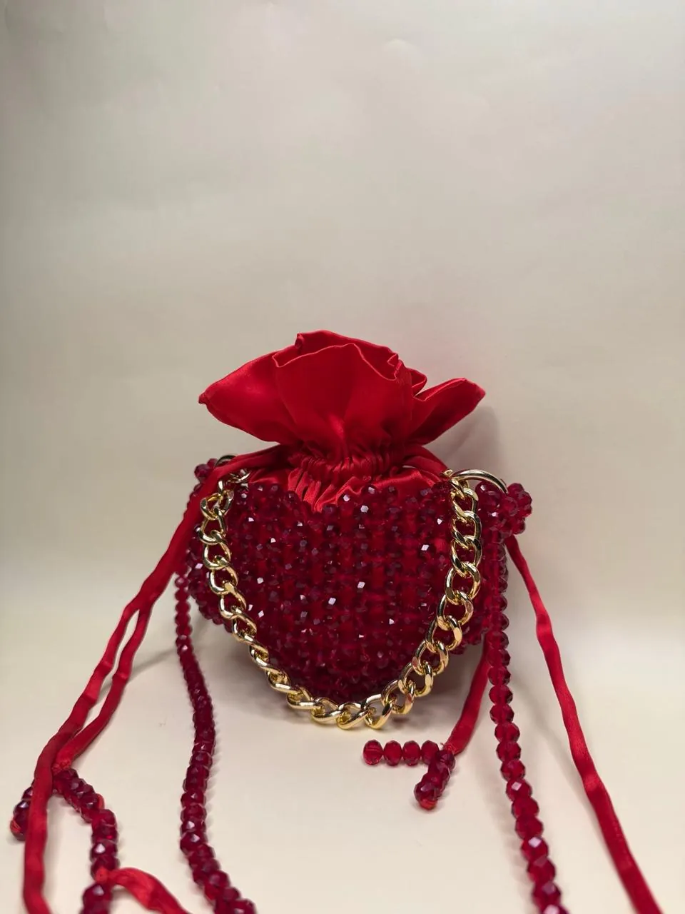 Red crystal-beaded drawstring bag with a gold chain handle and a satin top on a plain backdrop