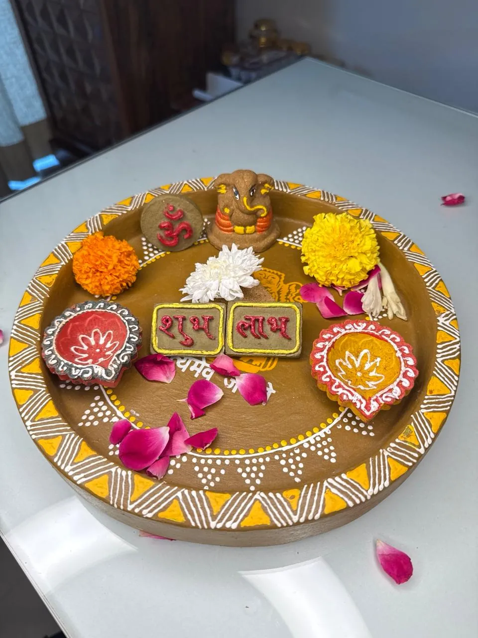 Painted terracotta puja thali with a clay Ganesha, an Om disc, Shubh Labh tiles, two diyas and marigold flowers